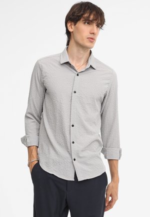 Camicia grigia chiaro a motivi con colletto button-down, maniche lunghe arrotolate e bottoni neri. Tessuto testurizzato con un design sottile.