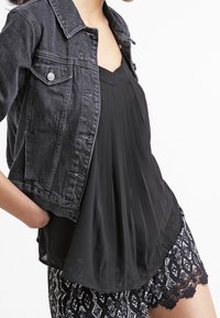 Svart denimjacka med silverdetaljer över en svart plisserad topp. Svarta mönstrade shorts med spetsdetaljer vid fållen.