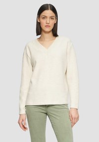 V-hals trui van zacht crèmekleurig breiwerk, met lange mouwen en een relaxte pasvorm, gecombineerd met lichtgroene slim-fit broek.
