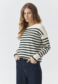 Sweter w paski w odcieniach kremowym i zielonym, wykonany z dzianinowego materiału. Charakteryzuje się luźnym krojem z opadniętymi ramionami oraz ściągaczami na mankietach.