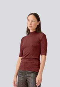 Burgundy ribbetoppi lyhyillä hihoilla ja korkealla kauluksella, valmistettu pehmeästä kankaasta, vartalonmyötäinen malli hienovaraisella tekstuurilla.