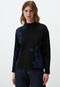 Zwarte trui met een hoge hals, voorzien van een bloemenpatroon in marineblauw aan één kant. Het materiaal lijkt zacht met een ontspannen pasvorm.