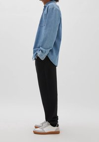 Ljusblå denimskjorta med knappar och bröstficka, i kombination med svarta sweatsbyxor och vita sneakers med grå och bruna accenter.