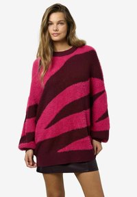 Pūkains pārspīlēti liels džemperis ar izteiktiem rozā un bordo svītrām, apaļu apkakli un ribota tipa aprocēm. Tekstūrētā auduma sastāvs piešķir maigumu.