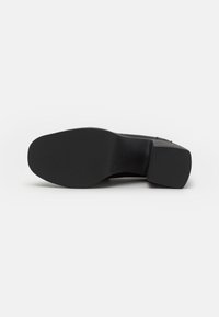 Suela de goma negra con una superficie texturizada. Diseño de tacón en bloque distintivo y parte superior suave para mayor estabilidad. Forma y acabado minimalistas.