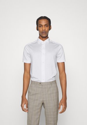 Chemise blanche à manches courtes et col étalé, associée à un pantalon à carreaux marron clair avec une coupe ajustée et une poche avant.