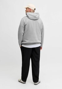 Hellgrauer Pullover mit Kapuze, getragen über einem weißen Hemd, kombiniert mit schwarzen Hosen und hellen Sandalen. Minimalistisches Design und Textur.