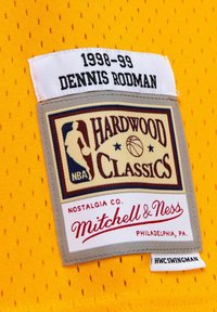 Tissu de maillot de basketball jaune avec une texture en maille ; étiquette cousue indiquant "Hardwood Classics, Dennis Rodman, 1998-99" dans différentes polices et couleurs.