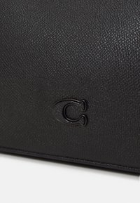 Surface en cuir texturé noir avec une lettre « C » noire brillante en relief embossée près du bord inférieur central.