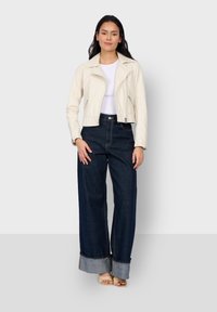 Crème neplederen jasje met een opstaande kraag en ritsen, gecombineerd met hoge taille wijde spijkerbroek in donkerdenim, voorzien van opgerolde boorden.