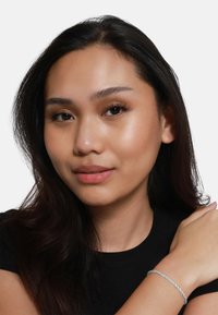 Bracciale d'argento con design attorcigliato, indossato su un polso contro un top nero. Texture liscia con dettagli intricati.