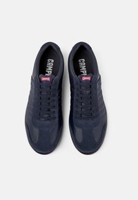 Tenisi bleu marin cu un design din materiale mixte, având piele netedă și suede texturat, vârf rotund și şireturi plate. Brandingul "Camper" este vizibil.