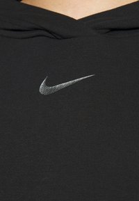 Svart sweatshirt med en texturerad silverfärgad Nike-swoosh-logotyp på bröstet. Tyget är slätt och ribbat med en strukturerad huva.