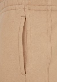 Nahaufnahme von beigem Strickstoff, der eine vertikale Seitentasche mit detaillierten Stichen auf einem Kleidungsstück zeigt.
