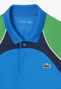 Blå och grön polotröja med slim fit, med en texturerad kropp, treknapplåsning och broderad logotyp. Designen inkluderar kontrasterande paneler.