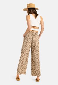 Pantaloni cu croi larg, cu un model maro și un design floral crem. Confectionați dintr-un material ușor. Așezați cu un top scurt alb și sandale bej.