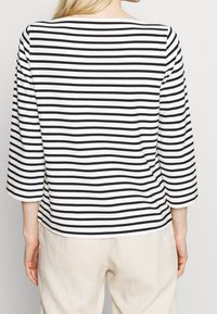 Black and white striped long-sleeve top, with a boat neck and three-quarter sleeves, made from soft fabric. Accentuated by horizontal stripes.