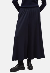 Marineblauwe wijde broek van een gladde stof, met een elastische tailleband en een vloeiende silhouet, gecombineerd met zwarte instappers.