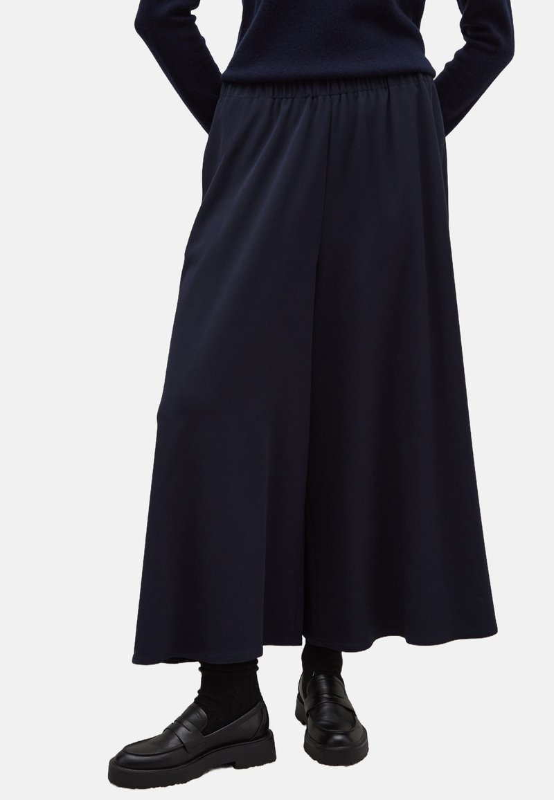 Marineblauwe wijde broek van een gladde stof, met een elastische tailleband en een vloeiende silhouet, gecombineerd met zwarte instappers.