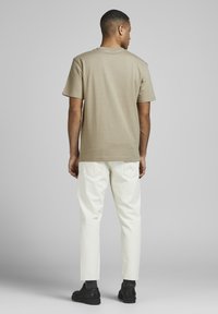 Cotton t-shirt in beige, classic crew neck, short sleeves. Paired with white pants and black shoes, showcasing a relaxed fit.