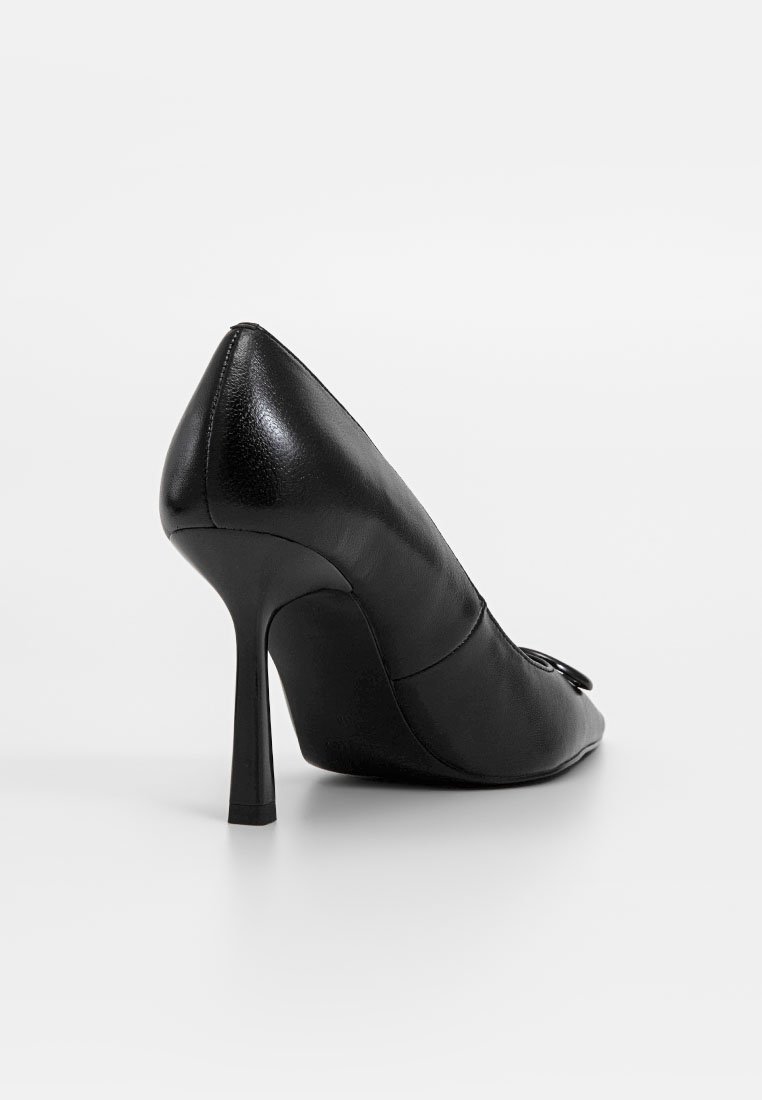 Czarna skórzana szpilka z wąskim noskiem, gładką teksturą i ozdobnym detalem w postaci kokardy z przodu. Projekt obcasa typu stiletto.