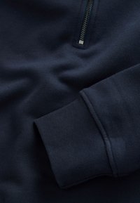 Marineblauwe sweatstof met een geribde mouw en een korte zilveren rits op het borstgebied.