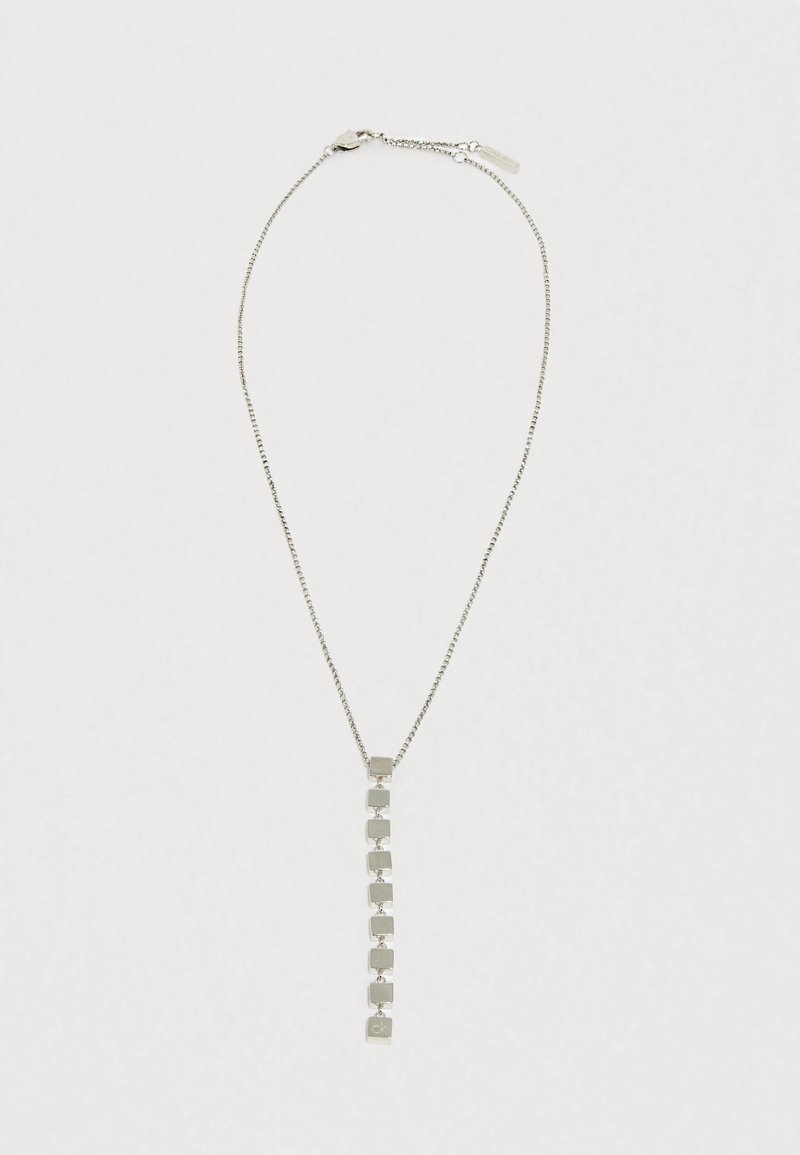 Sidabrinė apyrankė su grandinėle ir vertikaliu pakabuku, pagamintu iš kvadratinių grandinėlių, su maža logotipo etiketė gale.