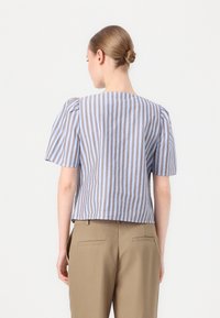 Blouse rayée en bleu clair et marron, avec des manches bouffantes courtes et un col rond, associée à un pantalon beige ajusté.