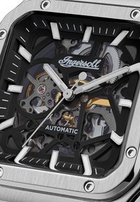 Automatic watch with a square stainless steel case, transparent black dial, silver hands, and exposed inner mechanisms. Features Ingersoll branding.