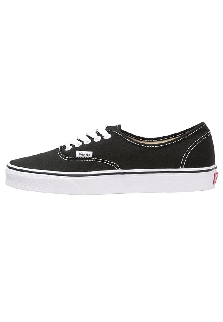 Baskets basses Vans noires avec lacets blancs, semelle blanche et logo de la marque visible sur le côté et à l’arrière du talon.