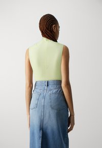 Lys grønn ermeløs bodysuit med en tettsittende design, parret med et høyhaltet denimskjørt med baklommer og en lett flare.