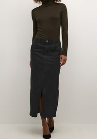 Jupe maxi en denim noir avec une fente à l'avant, deux poches et une fermeture à bouton. Associée à un top ajusté à manches longues marron.