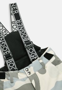 Sneeuwbroeken met zwarte bretels met het "BOGNER" logo, een camouflagepatroon in grijs en wit, een ritszak en drukknopsluitingen.