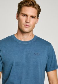 Μπλε κοντομάνικο μπλουζάκι φτιαγμένο από υφή βαμβάκι, με στρογγυλή λαιμόκοψη και μικρό λογότυπο σε σκούρο μπλε στην αριστερή περιοχή του στήθους.