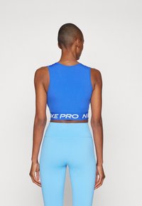 Blauw sport crop top met een witte "Nike Pro" band, gecombineerd met lichtblauwe, hoog uitgesneden leggings. Gladde stof en aansluitend ontwerp.