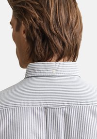 Gestreept shirt met een kraag die vastgeknopen kan worden en een plooi detail aan de achterkant. Het materiaal is lichtgewicht katoen met blauw-witte strepen.