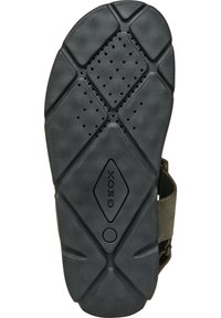 Semelle de chaussure en caoutchouc noir présentant un motif géométrique avec des trous de drainage, accentuée par une surface texturée et un logo circulaire au centre.