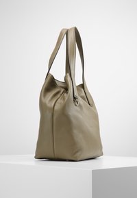 Torba na ramię z oliwkowej skóry o miękkiej fakturze, szerokim otwarciu i dwóch długich paskach. Projekt jest niestrukturalny, z widocznymi szwami po bokach.