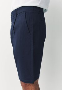 Granatowe bawełniane szorty z płaskim przodem, dwoma bocznymi kieszeniami i jedną tylną kieszenią. Charakteryzują się gładką fakturą i prostym krojem.