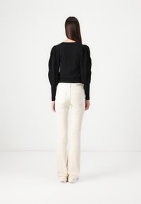 Haut noir avec manches bouffantes texturées ; pantalon évasé crème. La tenue présente une silhouette ajustée et un détail subtil d'encolure festonnée.