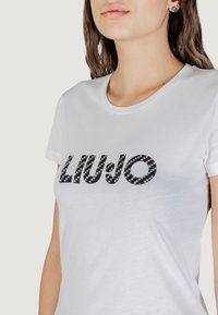 T-shirt bianca a maniche corte con logo "LIUJO" in paillettes nere sul davanti. Collo rotondo, materiale in cotone morbido e giusto in vita.