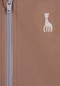 Tessuto marrone con una fine trama, dotato di una cerniera argento e un piccolo logo di giraffa ricamato in bianco sul lato destro.