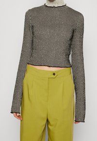 Top a maniche lunghe a righe bianche e nere con un colletto alto, abbinato a pantaloni verdi a vita alta con un singolo bottone.