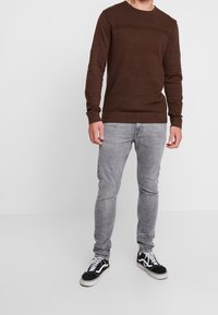 Suéter marrón de punto con un patrón texturizado, combinado con jeans ajustados grises y zapatillas negras con cordones blancos.