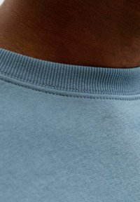 Camiseta de algodón azul claro con cuello redondo acanalado, que presenta una textura suave y costuras precisas a lo largo del cuello y el dobladillo.