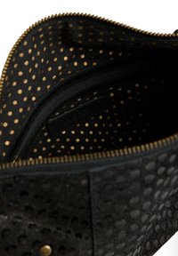 Sac zippé noir avec un intérieur à motif à pois dor és, un extérieur texturé avec un design perforé et une étiquette en cuir.