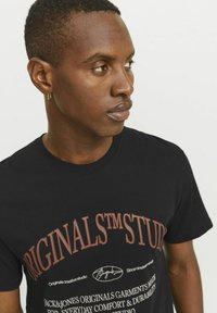 Zwart T-shirt met korte mouwen, voorzien van vetgedrukte, meerkleurige tekst en een ronde halslijn. De stof lijkt glad en lichtgewicht.