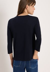 T-shirt bleu marine à manches longues avec un col rond. Matériau doux avec une texture lisse et une coupe décontractée. La vue arrière montre des détails de couture.
