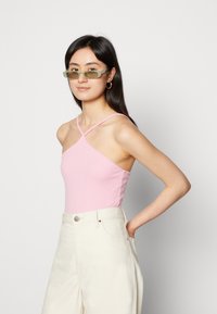 Bodysuit rosa com textura em canalé, apresentando um decote assimétrico único e alças finas, combinado com calças largas de cintura alta em tom creme.