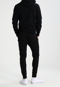 Svart huvtröja med en framfickor i känguru-stil, ribbade muddar och justerbar dragsko. Kombinerad med svarta joggers och vita sneakers.